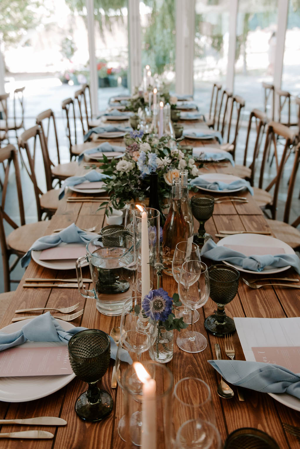 wooden wedding tables with candles set with white plates blush menus and blue napkins