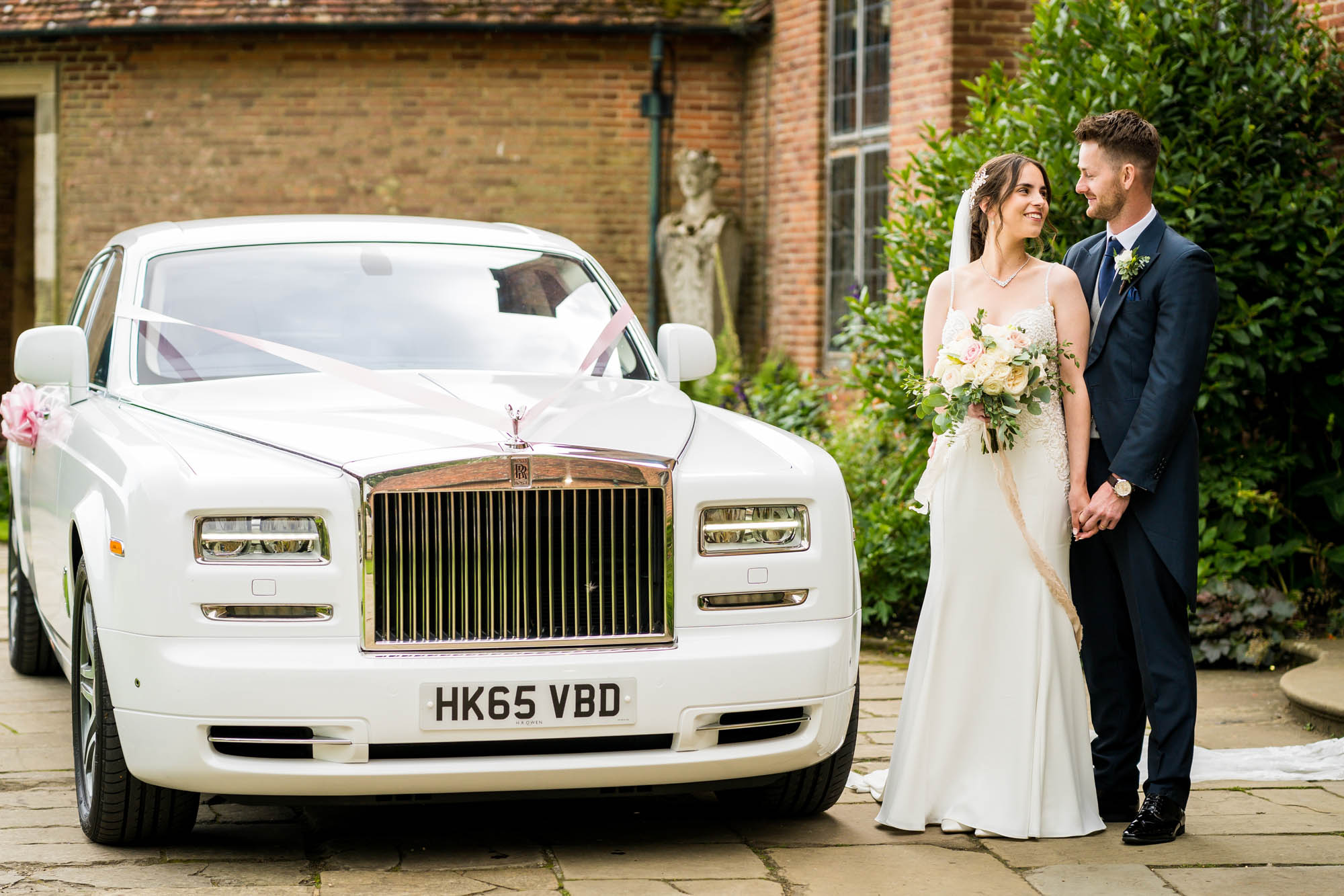 Luxury Rolls Royce in White with a bride and groom stood to one side of the car. By Benjamin Toms Photography in Kent