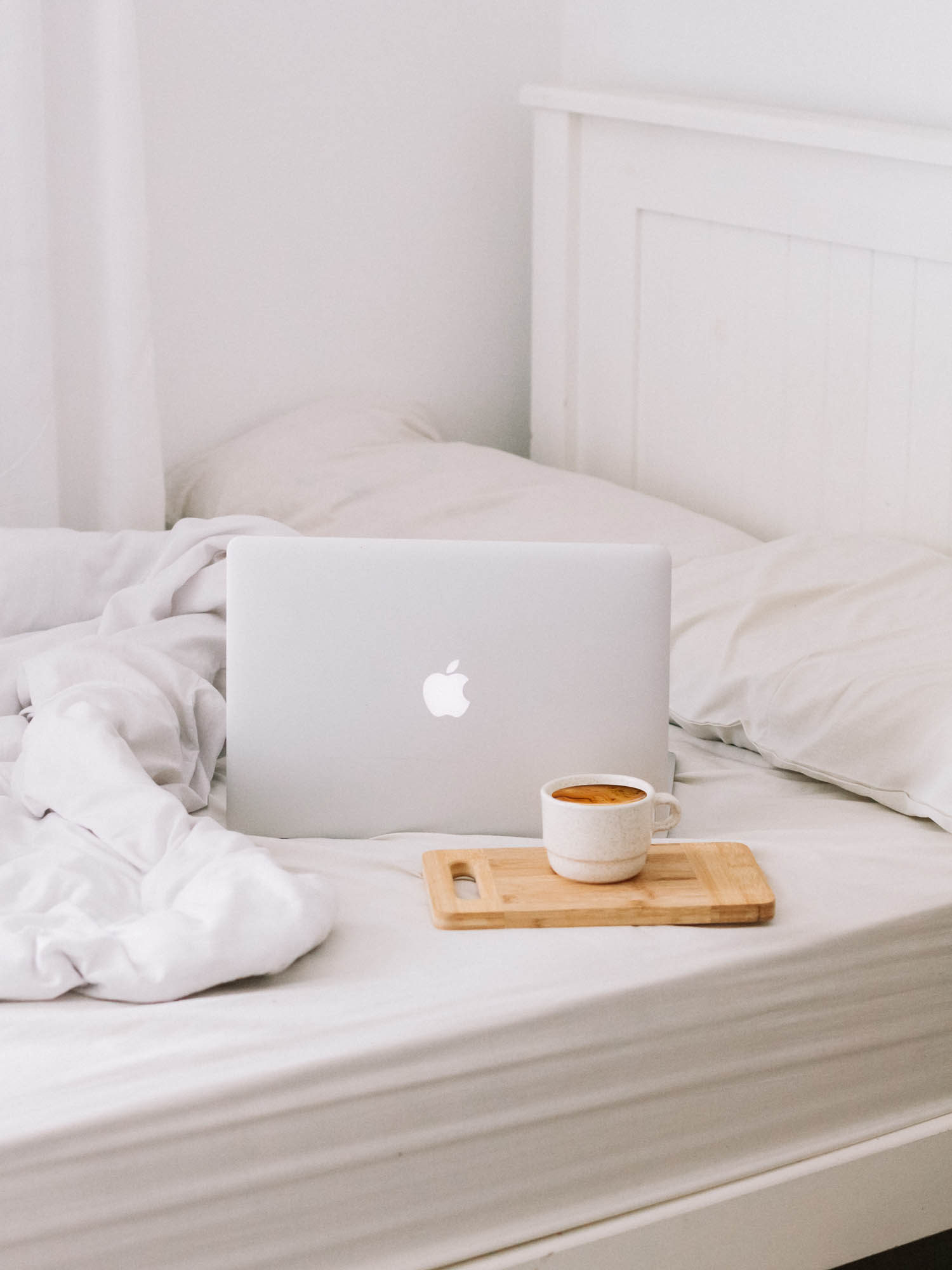a coffee and a MacBook on a white bed with the duvet rumpled up